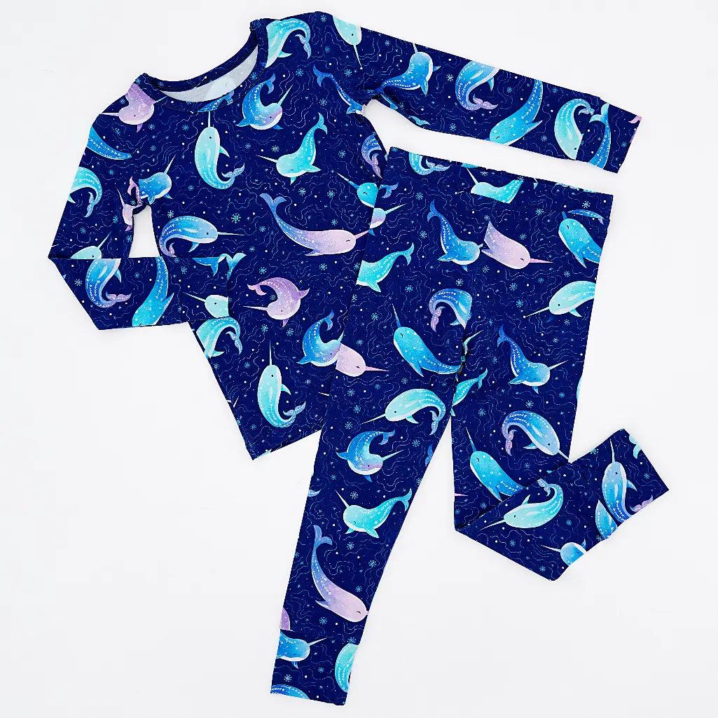 Flat lay of a long sleeve pajama top and matching pants in a royal blue print of blue and lavender narwhals on a white background.