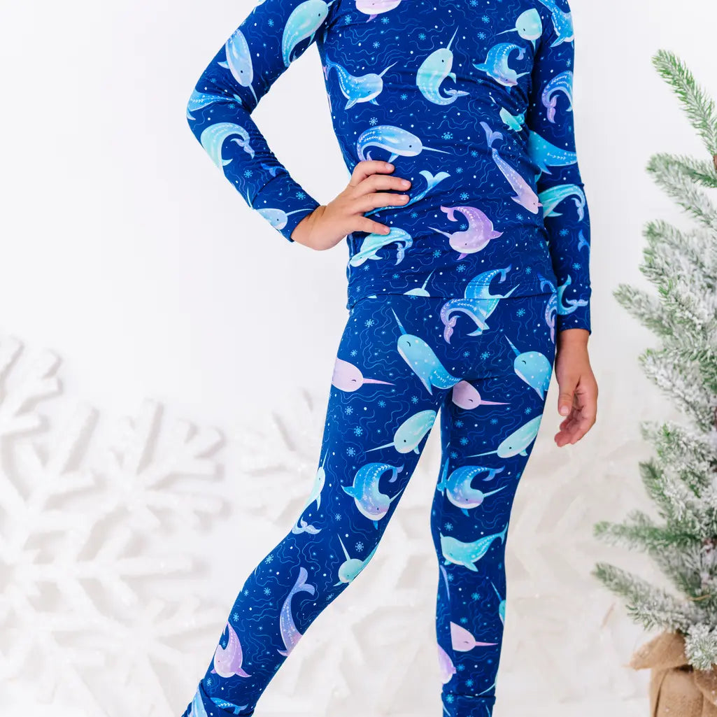 Close up of a child with a hand on the hip, showing the hem of a long sleeve pajama top and matching pants in a royal blue print of blue and lavender narwhals.
