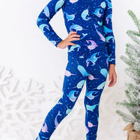 Close up of a child with a hand on the hip, showing the hem of a long sleeve pajama top and matching pants in a royal blue print of blue and lavender narwhals.