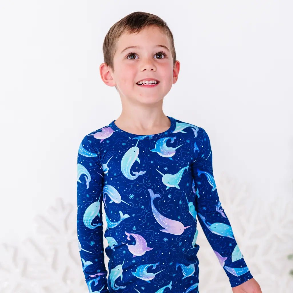 Close up portrait of a child looking up with a smile, in a long sleeve pajama top in a royal blue print of blue and lavender narwhals.