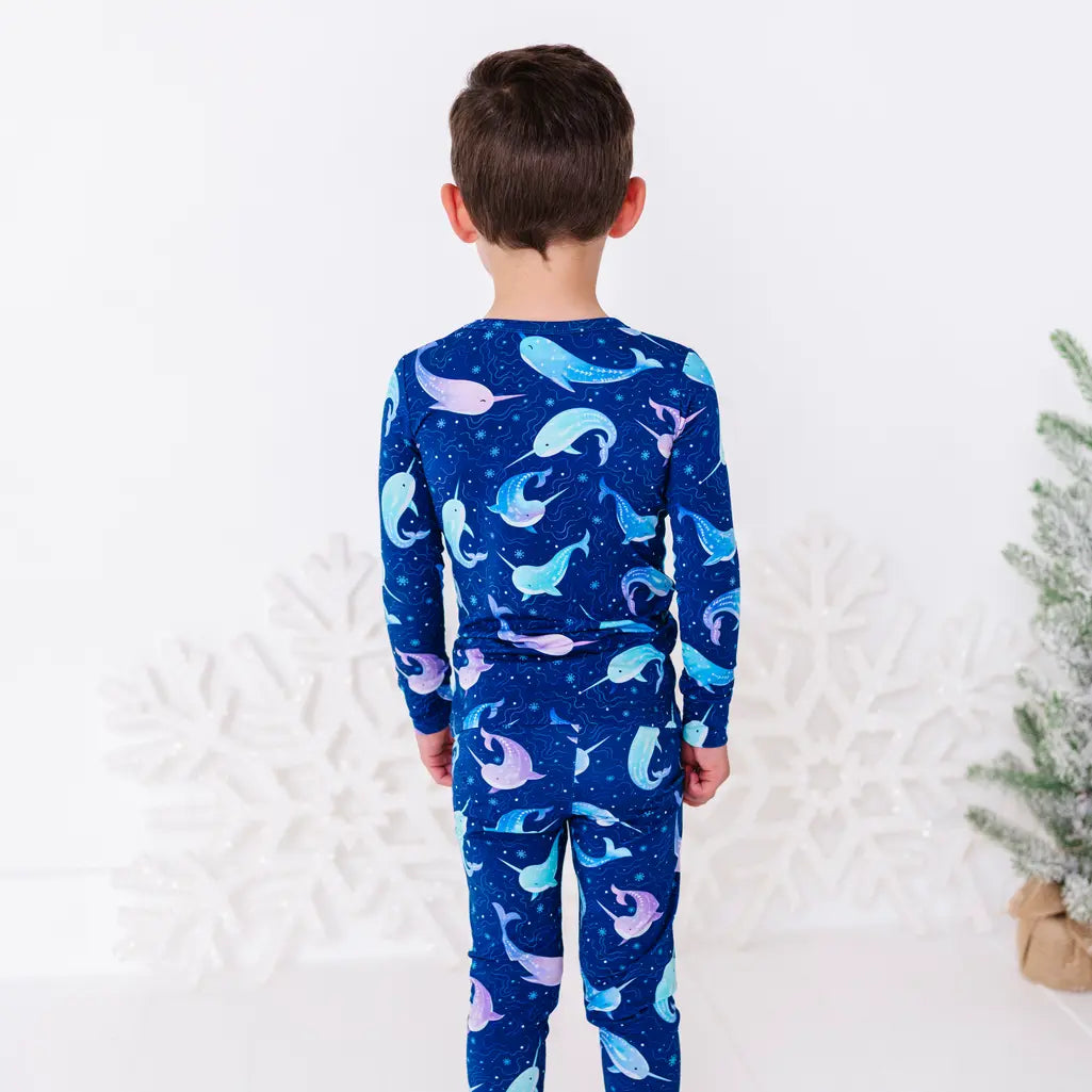 Back view of a child standing in a long sleeve pajama top and matching pants in a royal blue print of blue and lavender narwhals.
