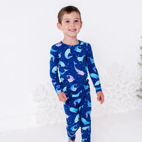 A child stepping forward with a smile, in a long sleeve pajama top and matching pants in a royal blue print of blue and lavender narwhals.