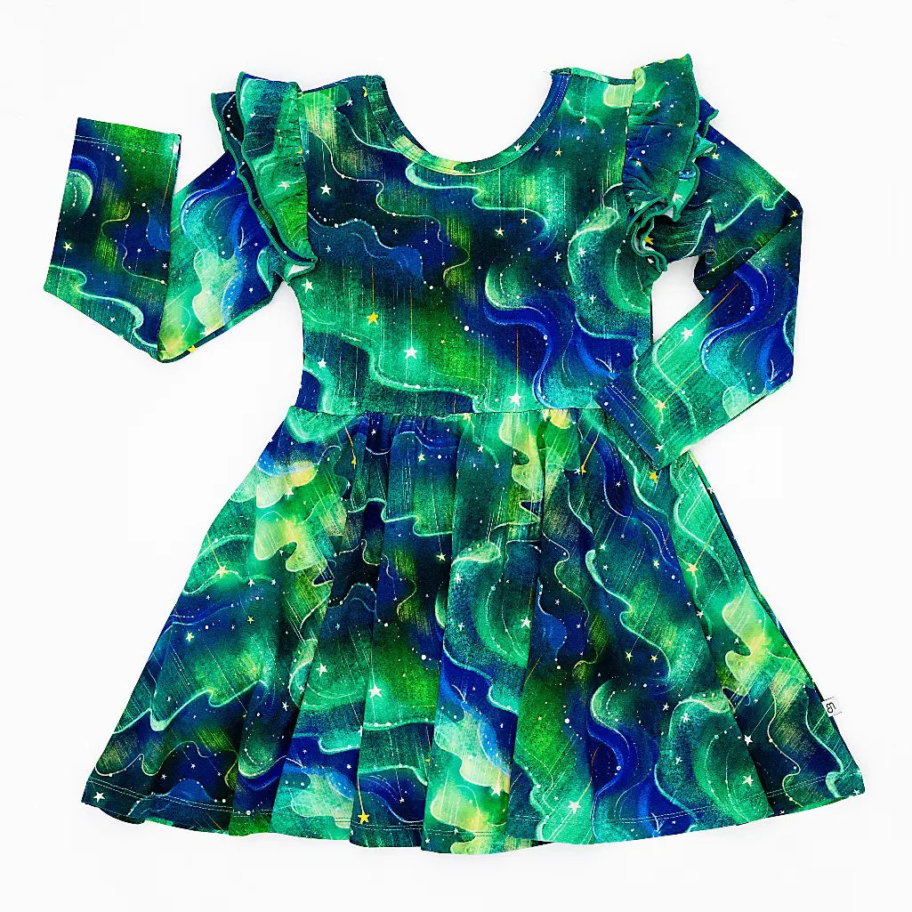 Flat lay of a long sleeve twirl dress with flutter ruffles at the shoulders in a green and blue northern lights print with tiny stars on a white background.