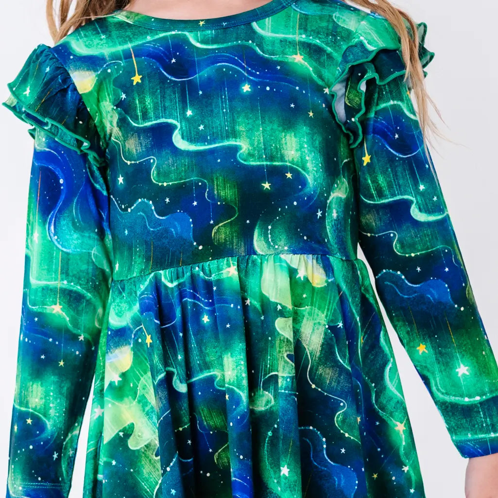 Close up of the front of a long sleeve twirl dress with flutter ruffles at the shoulders in a green and blue northern lights print with tiny stars.