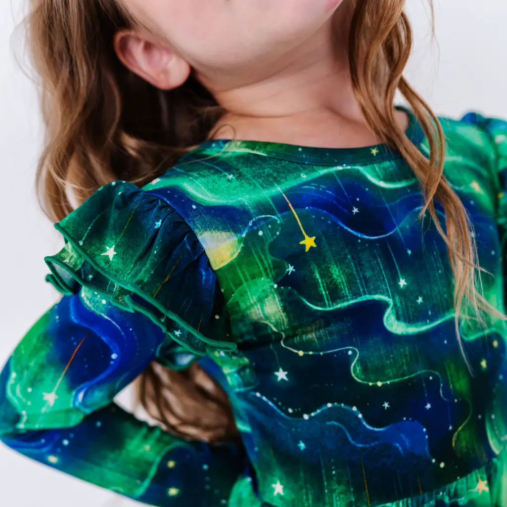 Close up of a flutter ruffle on the shoulder of a long sleeve twirl dress, showing a green and blue northern lights print with tiny stars.