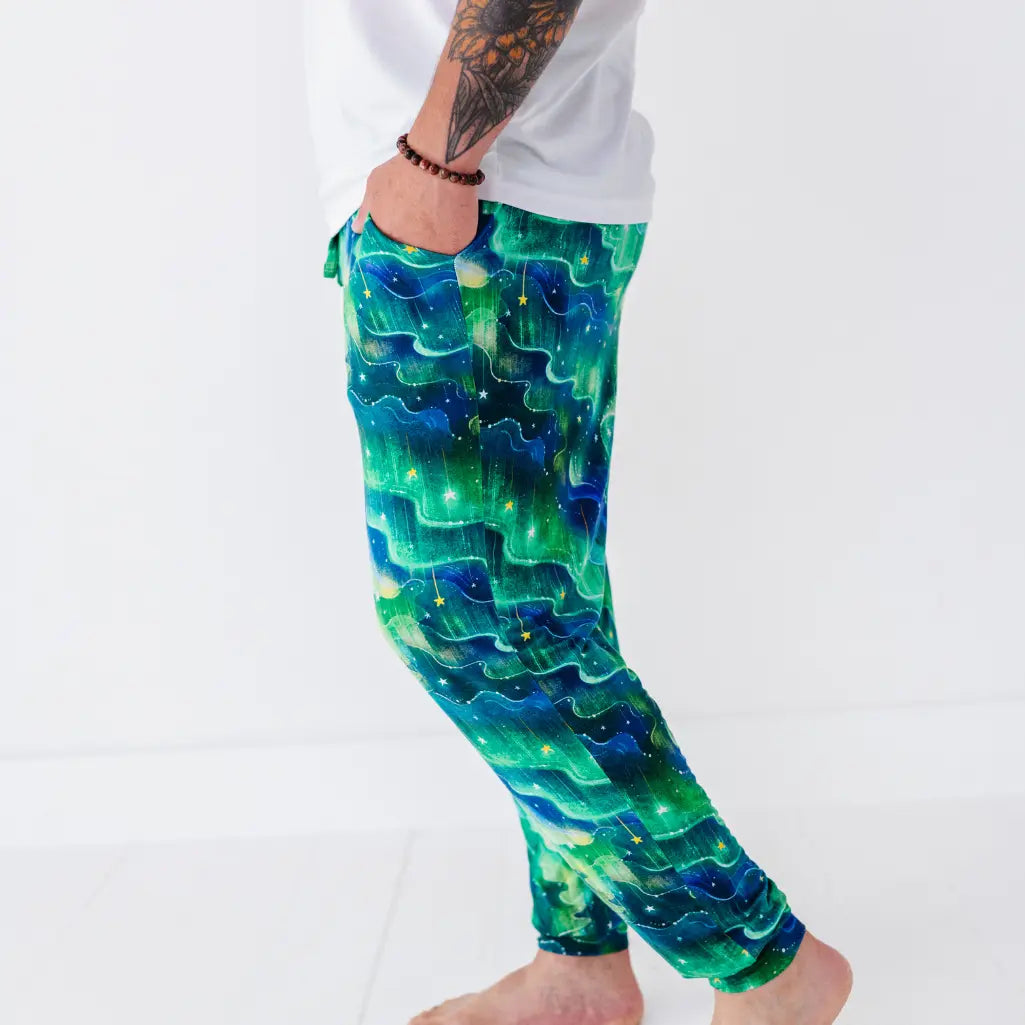 Side view of a man wearing jogger pajama pants with a swirling green and blue northern lights and stars pattern.