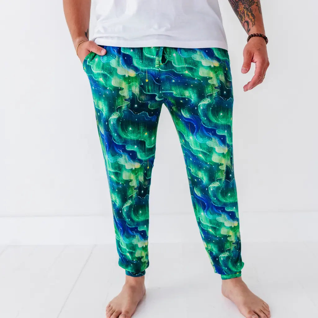 Front view of drawstring jogger pajama pants with a green and blue northern lights pattern and scattered stars.