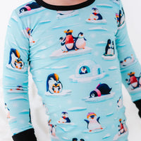 Close up of the chest and sleeves of a long sleeve pajama top with black cuffs in a light blue print of penguins playing on ice floes.