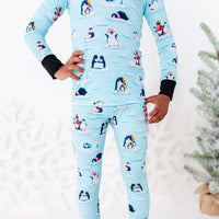 Close up of a long sleeve pajama top and pants with black cuffs and a hand on the hip, shown from the chest down to the thighs, in a light blue print of penguins playing on ice floes.