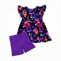 Flat lay of a flutter sleeve peplum top in a black watercolor floral print with purple bike shorts on a white background.