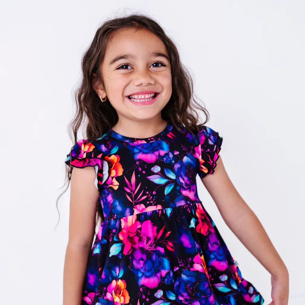 Close up portrait of a laughing child with the head tilted, in a flutter sleeve peplum top in a black watercolor floral print.