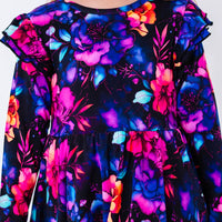 Close up of the front of a long sleeve twirl dress with flutter ruffles at the shoulders in a black print of pink, orange, purple, and blue watercolor flowers.