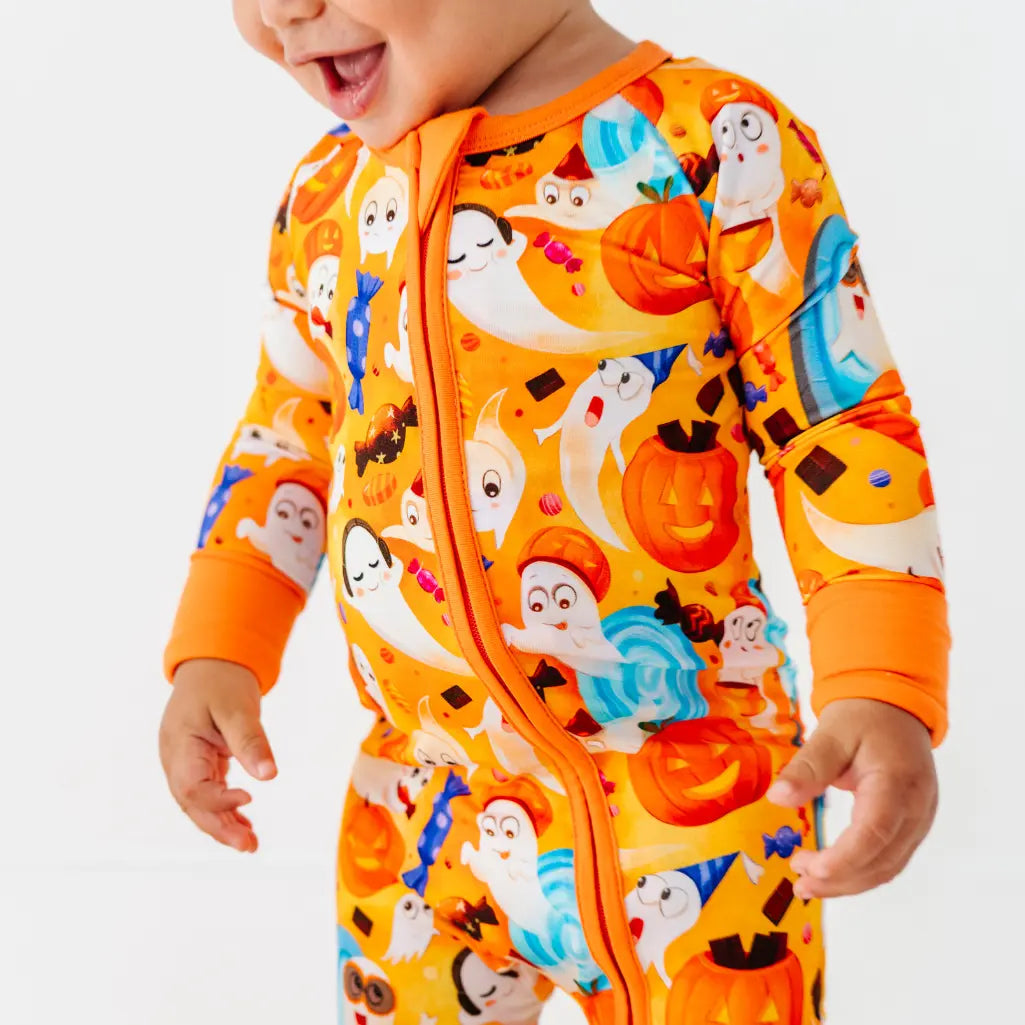 Close-up of a baby wearing an orange zip-up pajama covered in friendly ghosts, jack-o-lanterns, and candy.