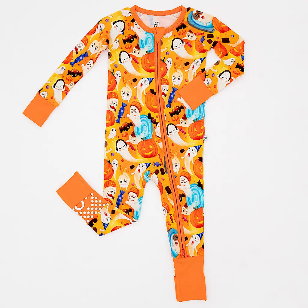 Flat lay of an orange zip-up convertible baby pajama with a friendly ghost, pumpkin, and candy print on a white background.