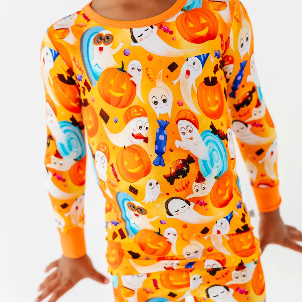 Close-up of a child wearing an orange two-piece pajama set covered in friendly ghosts, jack-o-lanterns, and candy.