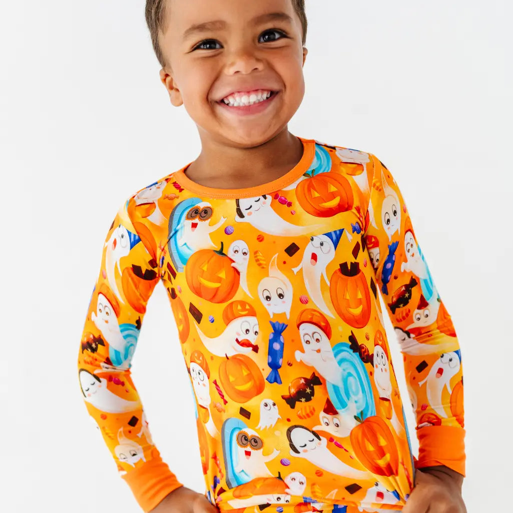 A smiling child wearing an orange long sleeve pajama top with a friendly ghost, pumpkin, and candy print.