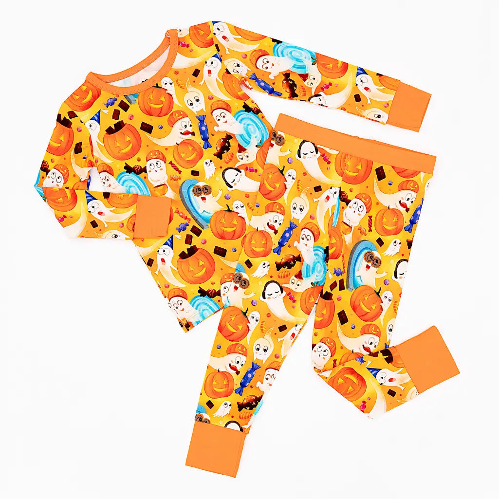 Flat lay of an orange two-piece pajama set with a friendly ghost, pumpkin, and candy print on a white background.