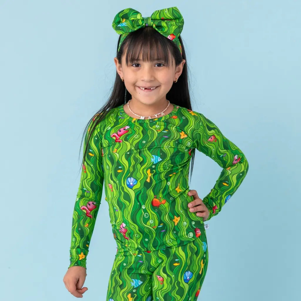 Child wearing a green patterned outfit with a matching headband on a light blue background