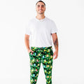 A man in a white tee standing with his hands in the pockets of dark green pajama pants with a colorful tree frog print.