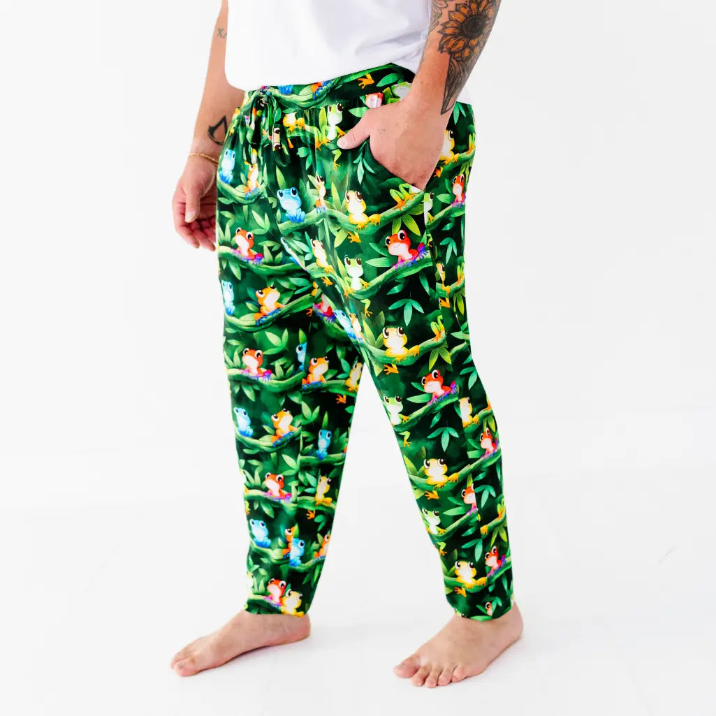 Side view of a man wearing dark green jogger-style pajama pants with a colorful tree frog and jungle vine print.