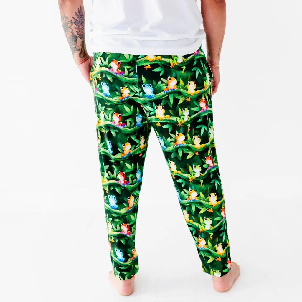 Back view of a man wearing dark green pajama pants with a colorful tree frog and jungle leaf print.