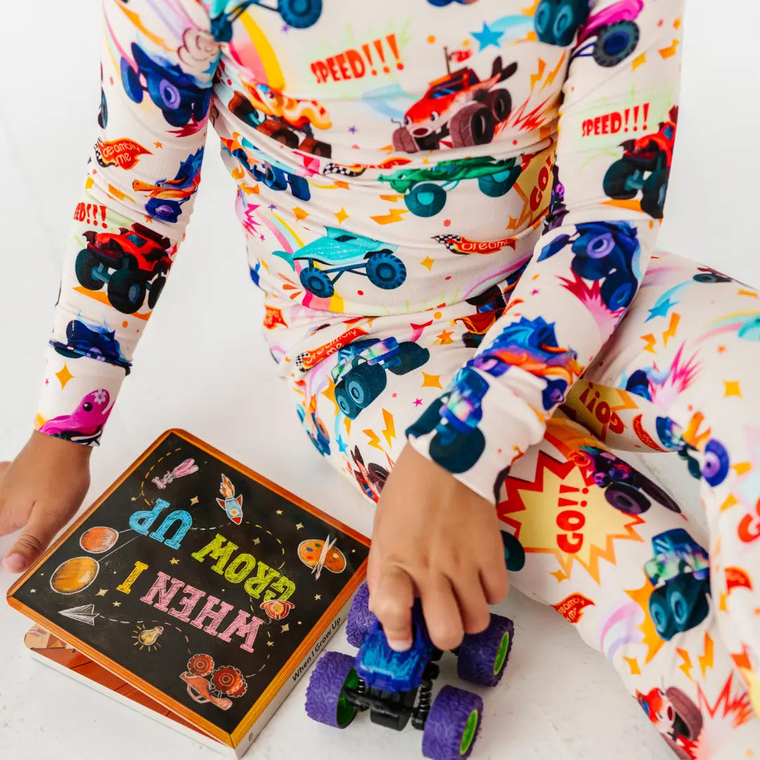 A child sitting on the floor in monster truck print pajamas, holding a toy truck next to the When I Grow Up storybook.