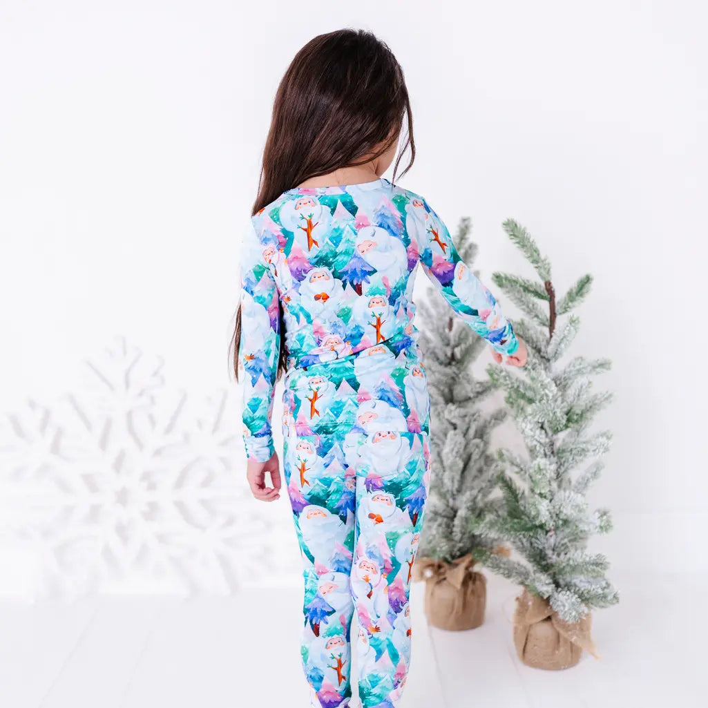 Back view of a child in a long sleeve pajama set with a print of friendly white yetis among teal, blue, and purple pine trees, reaching toward a small frosted tree.