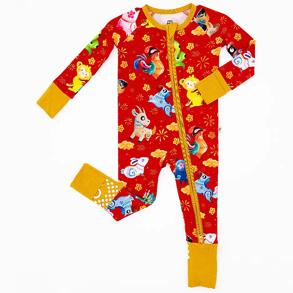 Flat lay of a zip up convertible baby pajama with mustard yellow trim and cuffs in a red print of zodiac animals and gold clouds on a white background.