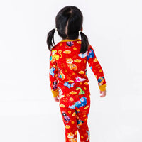 Back view of a child turning the head to one side, in a long sleeve pajama top and matching pants in a red print of zodiac animals and gold clouds.